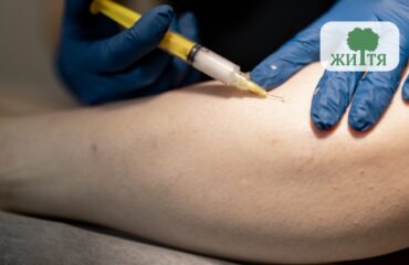 Medical professional in blue gloves administers an injection into a forearm; clinical setting.