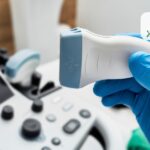 Yaki symptomy vkazuyut na potrebu v UZD sudyn zapamorochennya shum u vukhakh oniminnya | Медичний центр "Життя" Gloved hand holding an ultrasound probe over an ultrasound machine. Updated monitor and controls visible in the background.